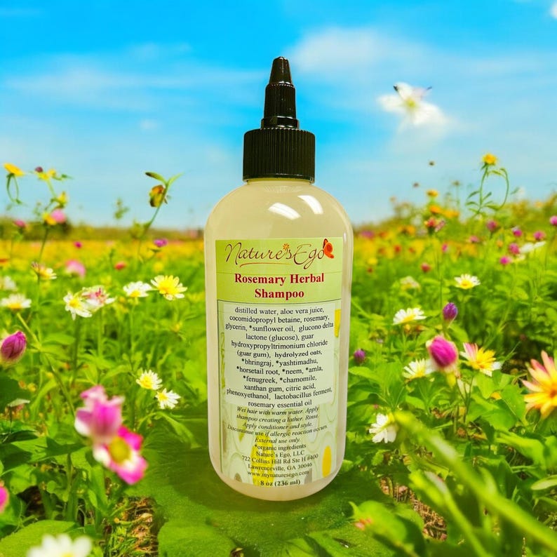 May include: A clear glass bottle of Nature's Ego Rosemary Herbal Shampoo with a black cap and label. The bottle is sitting on a bed of green grass and flowers.