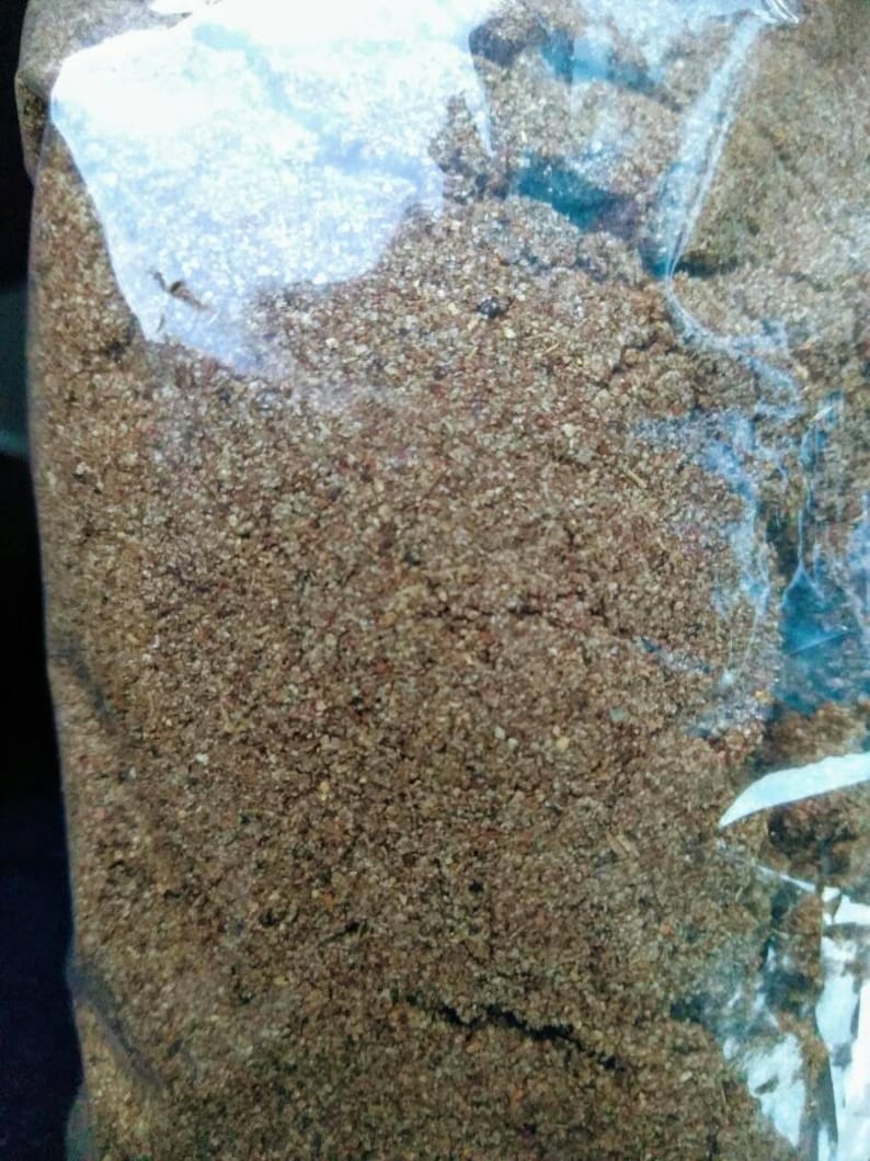 May include: A close-up of a brown, granular substance in a clear plastic bag. The substance appears to be a type of spice or seasoning.