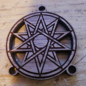 May include: A wooden pendant with a carved eight-pointed star design. The pendant has two holes on the top and bottom for attaching a chain or cord.