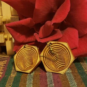 May include: A pair of wooden earrings with a spiral design. The earrings are a light brown color and have a gold-colored hook.