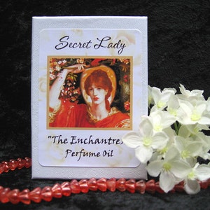 Może przedstawiać: Białe pudełko z kwiatowym wzorem i tekstem "Secret Lady" i "The Enchantress Perfume Oil".
