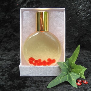 May include: A clear glass bottle with a gold cap and red hearts inside. The bottle is in a white box with a white background.