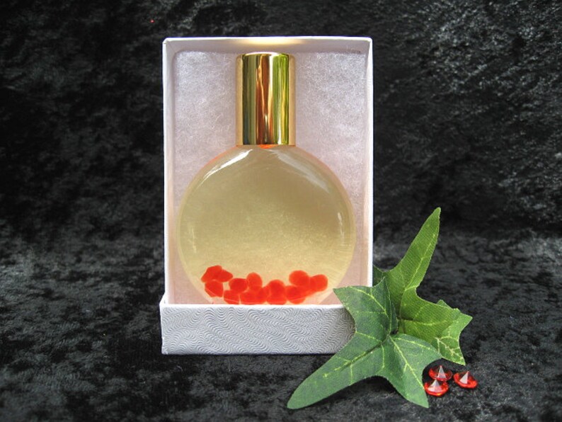 May include: A clear glass bottle with a gold cap and red hearts inside. The bottle is in a white box with a white background.