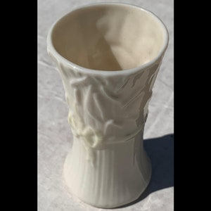 May include: A small, white ceramic vase with a floral design. The vase has a wide mouth and a narrow base.