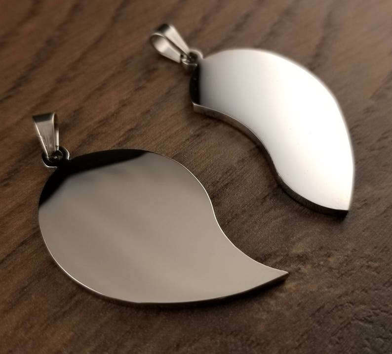 Puede incluir: Dos colgantes de plata con forma de mitades de coraz&oacute;n. Los colgantes son lisos y brillantes, y tienen un dise&ntilde;o simple y elegante.