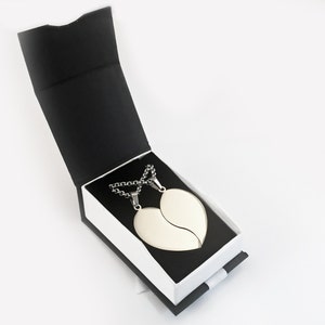 Puede incluir: Dos collares de plata con colgantes en forma de coraz&oacute;n, una mitad del coraz&oacute;n en cada collar, en una caja de regalo negra y blanca.