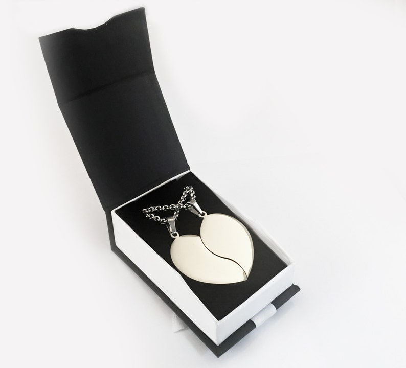 Puede incluir: Dos collares de plata con colgantes en forma de coraz&oacute;n, una mitad del coraz&oacute;n en cada collar, en una caja de regalo negra y blanca.