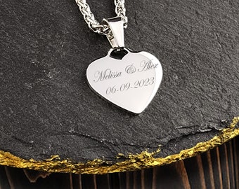 May include: Silver heart-shaped pendant necklace with a chain. The pendant is engraved with the names "Melissa & Alex" and the date "06-09-2023".