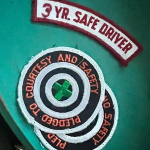 May include: A set of embroidered patches. One patch reads "3 YR. SAFE DRIVER" in white letters on a red and white curved background. Two circular patches are stacked, with the words "PLEDGED TO COURTESY AND SAFETY".
