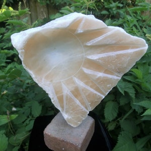May include: A white alabaster sculpture of a sun with a carved design. The sculpture is on a brown brick base.