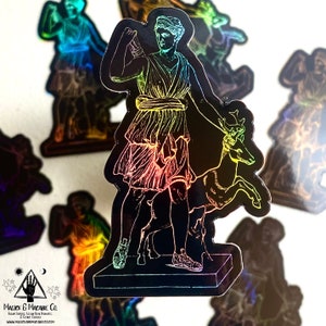 May include: A holographic sticker featuring a woman holding a deer. The woman is wearing a flowing robe and the deer is standing on its hind legs. The sticker is iridescent and has a rainbow effect.