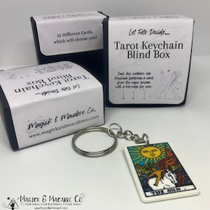 May include: A black box with white text that reads "Let Fate Decide... Tarot Keychain Blind Box". The box contains a keychain with a tarot card charm that shows "The Sun" card.