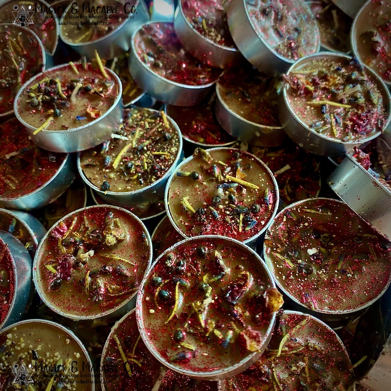 May include: A close-up of a pile of brown tea light candles with red glitter and dried herbs. The candles are in silver containers.