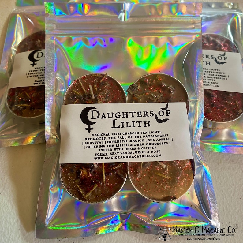 May include: Four brown tea lights with red glitter and herbs inside. The tea lights are packaged in a silver holographic bag with a white label that reads "Daughters of Lilith" and "Magickal Reiki Charged Tea Lights". The label also includes a description of the tea lights, including their purpose and scent. The label also includes the website address "www.magickandmacabreco.com".