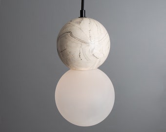 May include: A white ceramic pendant light with a textured, marbled finish. The light is suspended from a black cord and has a white frosted glass diffuser.