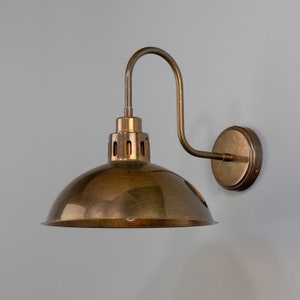 May include: A brass wall sconce with a curved arm and a dome-shaped shade. The shade has a distressed finish and a decorative ring around the top.
