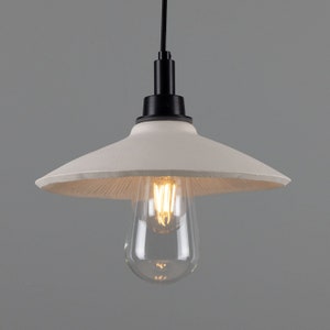 May include: A white pendant light with a black cord and a clear light bulb. The light fixture has a wide, flat, white shade.