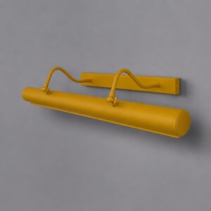 May include: A mustard yellow wall-mounted picture light featuring a long, cylindrical lamp head attached to a rectangular base plate by two curved, adjustable metal arms with visible pivot joints for directing the light beam downward.