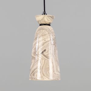 May include: A white ceramic pendant light with a marbled design. The light has a black cord and a black trim around the top.