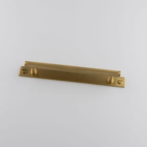 May include: A brass-toned cabinet pull featuring a textured, cylindrical handle and two smaller, rounded handles. The rectangular pull is set against a white backdrop.