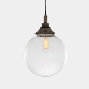 May include: A clear glass globe pendant light with a vintage-style Edison bulb. The light fixture has a dark metal cap and a black cord. The bulb is lit, emitting a warm, yellow glow. The overall design is simple and industrial.