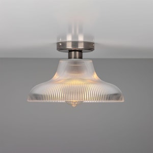 May include: A silver ceiling light fixture with a clear glass shade that has vertical lines. The light is on and illuminating the room.