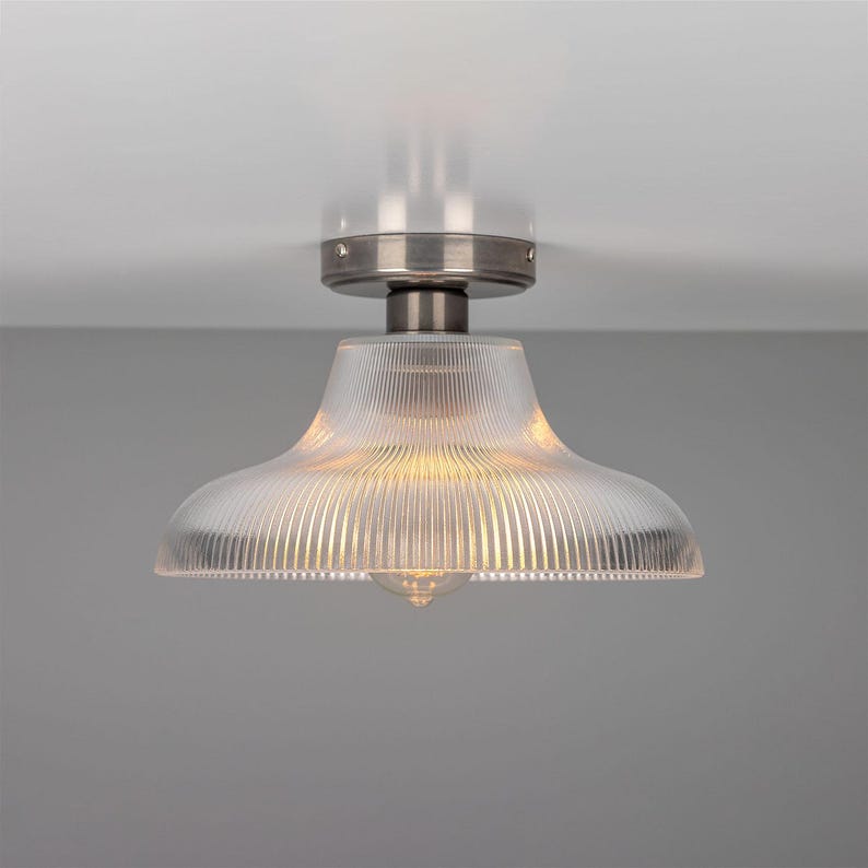 May include: A silver ceiling light fixture with a clear glass shade that has vertical lines. The light is on and illuminating the room.