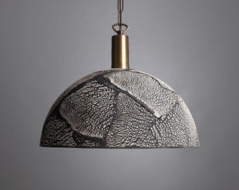 May include: A black and white ceramic pendant light with a textured, crackled finish. The light fixture has a brass chain and a brass dome-shaped ceiling mount.