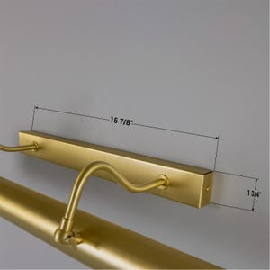 May include: A matte gold picture light with a rectangular wall-mounting base and an adjustable tubular lamp head. The base measures 15 7/8 inches in length, and the mounting bracket has a height of 1 3/4 inches, as indicated by technical lines.