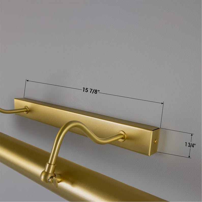 May include: A matte gold picture light with a rectangular wall-mounting base and an adjustable tubular lamp head. The base measures 15 7/8 inches in length, and the mounting bracket has a height of 1 3/4 inches, as indicated by technical lines.
