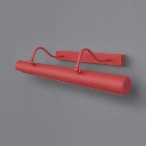 May include: A matte coral red picture light fixture featuring a long cylindrical lamp head attached to a rectangular wall-mounting plate by two curved, adjustable metal arms with visible pivot joints at the connection points.