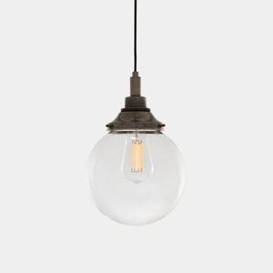 May include: A clear glass globe pendant light with a brass finish. The light is hanging from a black cord and has a single light bulb inside.