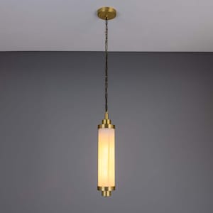 May include: A cylindrical pendant light fixture with a brass finish. The light has a frosted glass shade and hangs from a chain. The fixture is suspended from a brass ceiling mount.