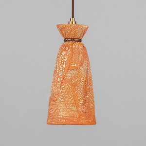May include: A terracotta pendant light with a crackled glaze finish. The light has a bell-shaped shade with a wide, flared top and a narrow bottom.