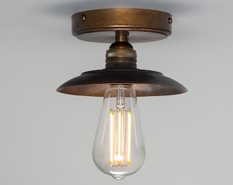 May include: A flush mount ceiling light fixture with a dark bronze finish. The fixture features a circular canopy, a short stem, and a wide, shallow dome-shaped shade. A clear glass Edison-style light bulb with visible vertical filaments is attached.
