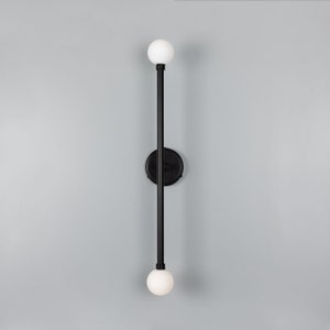 May include: A black wall sconce with two white globe light fixtures. The sconce has a long, vertical rod with a circular base.