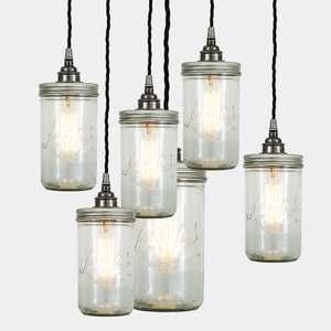 May include: A set of six clear glass mason jar pendant lights with silver lids and black electrical cords. The lights are hanging from the ceiling and are illuminated with light bulbs.
