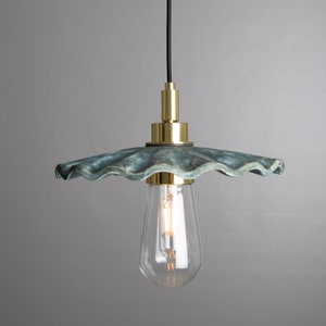 May include: A teal blue ceramic pendant light with a wavy, scalloped edge and a gold metal fixture. The light is hanging from a black cord and has a clear glass bulb.