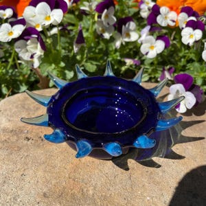 Peut inclure: Un petit plat en verre bleu cobalt avec un design en forme de soleil épineux. Le plat a un glaçage clair et iridescent et est parfait pour contenir de petites babioles ou des bijoux.