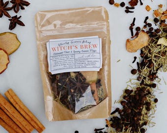 Könnte beinhalten: Ein durchsichtiger Kunststoffbeutel mit einer Herdplatten-Simmermischung mit der Aufschrift Witch's Brew. Der Beutel ist umgeben von losem Sternanis, getrockneten Apfelscheiben, Zimtstangen, Rosmarin, Nelken und Pimentbeeren auf weißem Grund.