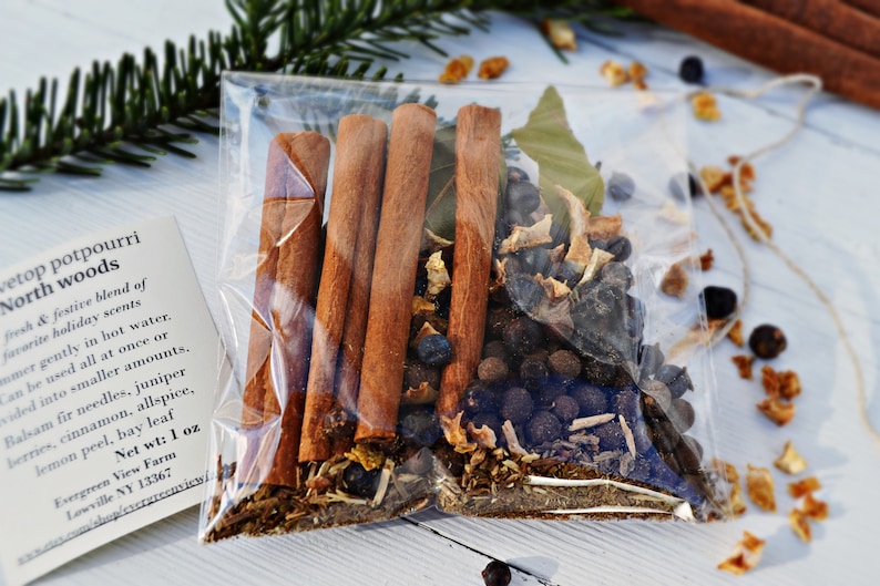 Pu&ograve; includere: Un sacchetto di plastica trasparente riempito con una miscela di ingredienti per pot-pourri, tra cui bastoncini di cannella, foglie di alloro, bacche di ginepro e scorza d'arancia. Il sacchetto &egrave; etichettato "North Woods Stovetop Potpourri" con un peso netto di 1 oncia.
