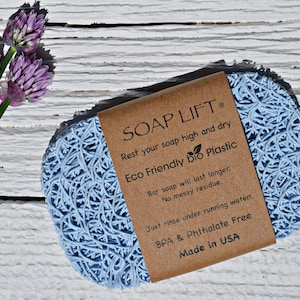 May include: A blue soap saver made of eco-friendly bio plastic. The soap saver is shaped like a disc and has a textured surface. The label reads "SOAP LIFT", "Rest your soap high and dry", "Eco Friendly bio Plastic", "Bar soap will last longer. No messy residue.", "Just rinse under running water!", "BPA & Phthalate Free", and "Made in USA".