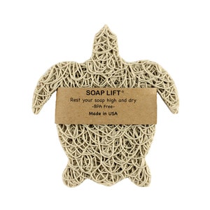 May include: A beige soap lift shaped like a turtle. The soap lift is made of woven material and has a brown label that reads "SOAP LIFT&reg; Rest your soap high and dry -BPA Free- Made in USA".