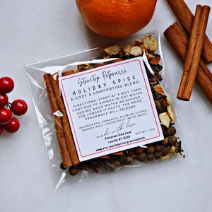 Pu&ograve; includere: Un sacchetto di plastica trasparente pieno di una miscela di spezie per pot-pourri da stufa. L'etichetta recita "Stovetop Potpourri Holiday Spice A Cozy & Comforting Blend" con istruzioni e ingredienti elencati. Il sacchetto &egrave; su una superficie bianca con un rametto di bacche rosse e un'arancia intera a lato.