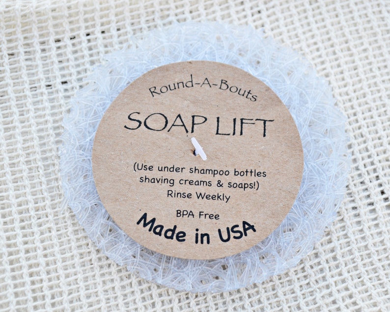 May include: A white mesh soap saver with a brown paper label that reads "Round-A-Bouts SOAP LIFT (Use under shampoo bottles shaving creams & soaps!) Rinse Weekly BPA Free Made in USA"