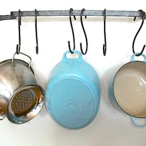 May include: A black metal pot rack with five hooks hanging from it. A blue pot, a white pot, and a silver colander are hanging from the hooks.