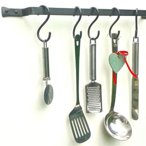May include: A black metal rack with six hooks holds a variety of kitchen utensils, including a spatula, grater, ladle, and pizza cutter.