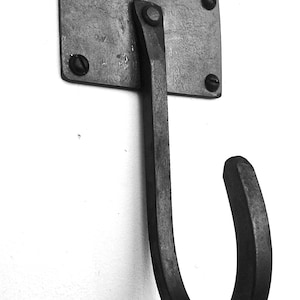May include: A black metal hook with a rectangular base and a curved hook. The hook is attached to a wall with screws.