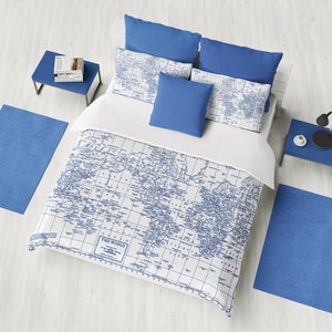 May include: A white duvet cover with a blue world map print. The duvet cover is on a bed with blue pillows and a white sheet. The bed is in a room with a white wooden floor and blue rugs.