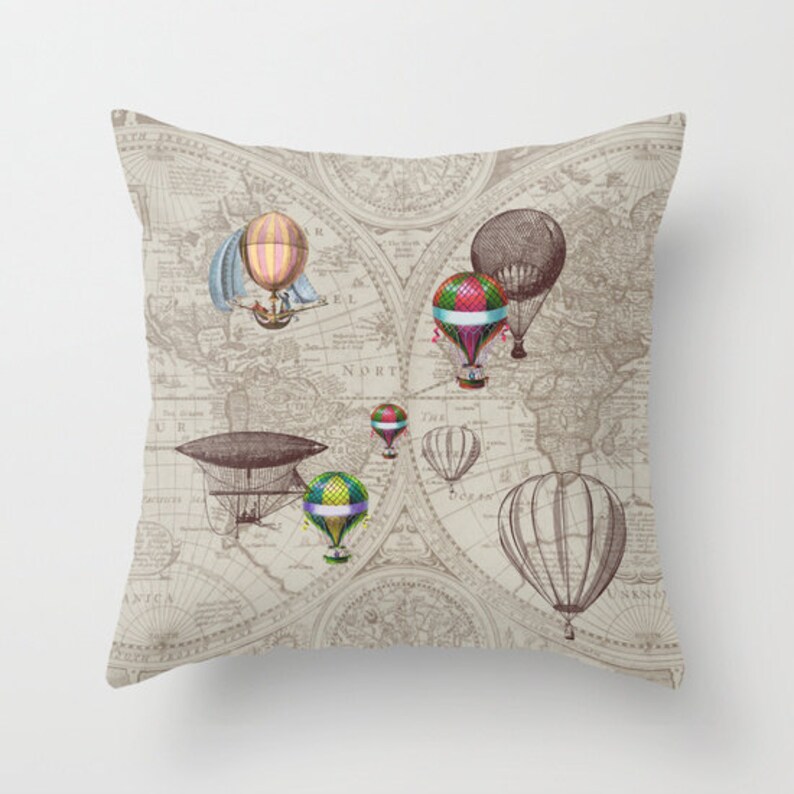 May include: A throw pillow featuring a vintage world map design with hot air balloons and an airship. The map is in shades of brown and beige with a cream background. The balloons are colourful and have a whimsical feel.